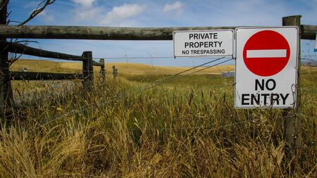 Landscape view of a farm land with wooden fence and warning signs. Lack of rain makes the grass appear yellow and dryの写真素材