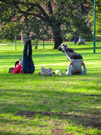 11 September 2018 - East Melbourne, Australia: Two women doing leg raise in the historical Fitzroy Gardens. The exercise is a form of bodyweight training. Calisthenics promote healthy lifestyle.のeditorial素材