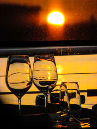 Wine glasses by a restaurant window with sun in the background. The sunlight creates backlight and silhouette of the objects on the dining table. Suitable as background image. Space for text availableの写真素材