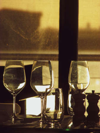 Wine glasses by a restaurant window with sun in the background. The sunlight creates backlight and silhouette of the objects on the dining table. Suitable as background image. Space for text availableの写真素材