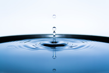 A drop of water fallling into blue water surfaceの写真素材