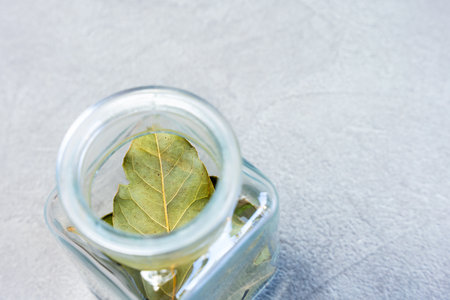 Glass jar with dried leaves on gray background. Culinary herb and natural seasoning.の写真素材
