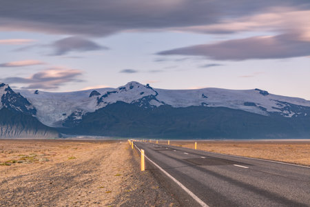 Open road leading to Icelandic glacier-covered mountains at duskの写真素材