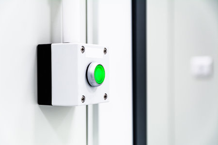 Green illuminated emergency stop button on white industrial wall