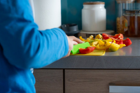 Person chopping red and yellow bell peppers on kitchen counter, showing home cooking, preparation and healthy lifestyle habitsの写真素材
