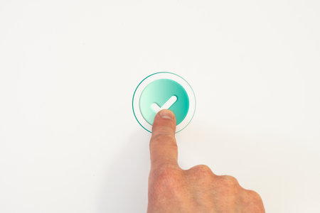 Hand pressing circular button with checkmark on white background, representing confirmation, acceptance, or validation in digital user interfaceの写真素材