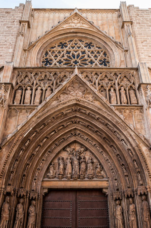 Gothic cathedral entrance with stone sculptures and stained glass rose window captured in vertical perspective for architectural history and culture visualsの写真素材