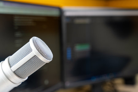 Condenser microphone in studio with blurred background screens showing audio editing software, ideal for podcasting visualsの写真素材