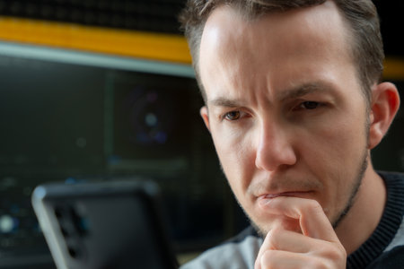 Focused man looking at smartphone in audio production studio with computer monitors and acoustic foam backgroundの写真素材