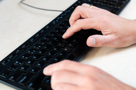 Top-down view of fingers pressing black keys on computer keyboard, workplace and technology context
