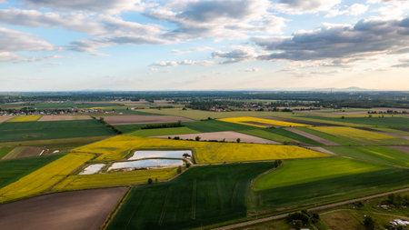 Aerial landscape of colorful agricultural fields with ponds under a partly cloudy sky at sunset, illustrating rural sceneryの写真素材
