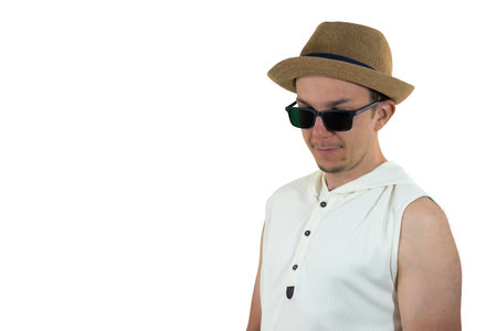 Young man in sunglasses and hat looking down with calm and reflective expression, isolated on white, casual summer portraitの写真素材