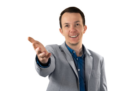 Smiling man in formal outfit reaching hand toward camera in a friendly welcoming gesture symbolizing invitation or partnership. Isolated portraitの写真素材