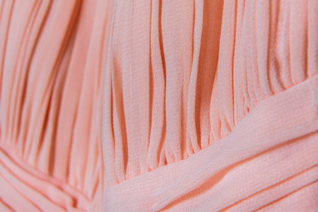 Detailed view of pleated peach fabric texture with soft lighting highlighting garment flow and feminine fashion conceptの写真素材