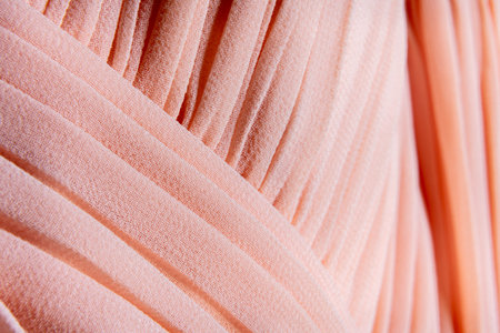 Peach-toned pleated fabric in macro with soft lighting and detailed texture for fashion and textile design applicationsの写真素材