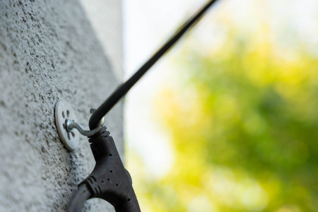 Cable mount detail on wall with power tool wire attached in outdoor setting with defocused green background, concept of home improvement and utilityの写真素材