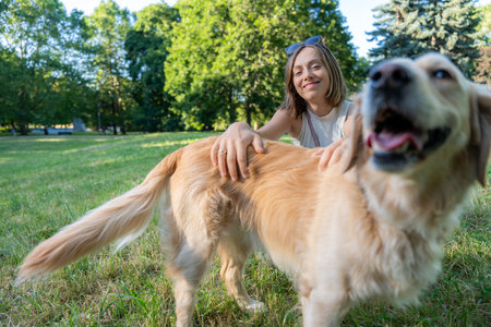 Woman smiling while petting golden retriever in park illustrating joyful connection with nature and petsの写真素材