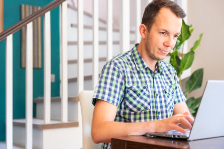 Focused Man Using Laptop While Working Remotely At Home Office Workspaceの写真素材