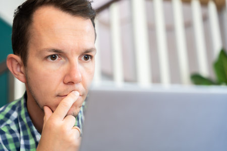 Thoughtful Man Holding Chin Looking At Laptop Screen At Home Office Remote Workの写真素材
