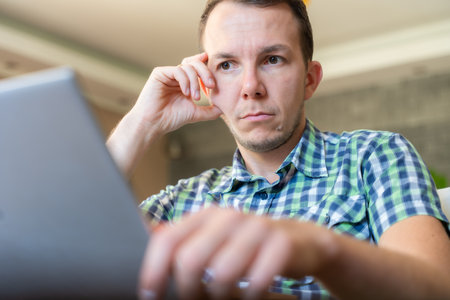 Serious Man Resting Head On Hand Focused On Laptop Screen Remote Work At Home Officeの写真素材