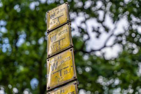Yellow Metal Utility Signs With Numbers And Letters Mounted Outdoors Against Green Trees Used For...