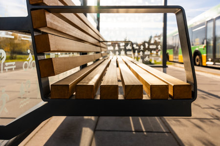 Modern Wooden Bench At City Bus Stop With Glass Shelter And Bus In Background, Comfortable Public Transport Waiting Areaの写真素材