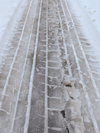 Car Tire Tracks In Icy Snow Covered Road Surface Creating Linear Winter Pattern And Slippery Transportation Backgroundの写真素材