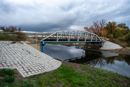 Steel Bridge Over Calm River With Sloped Concrete Embankment In Cloudy Weather For Infrastructure Useの写真素材