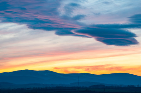 Colorful Sunset Sky Over Mountain Silhouette With Dramatic Layered Lenticular Clouds And Evening Glowの写真素材