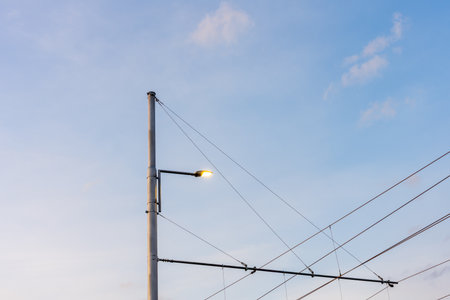 Street Lamp And Overhead Tram Wires Against Soft Blue Sky In Urban Transportation Infrastructureの写真素材