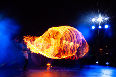 Fire Show Performance With Bright Orange Flames And Motion Trails On Dark Blue Stage Background. Creative Long Exposureの写真素材