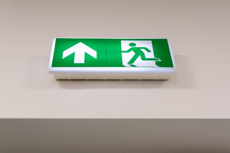 Green Emergency Exit Sign With Running Figure And Arrow On Indoor Wallの写真素材