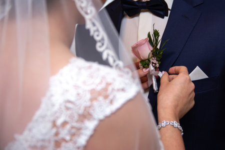 Bride Adjusting Groom's Pink Rose Boutonniere During Wedding Ceremony Preparation. Close-up Momentの写真素材