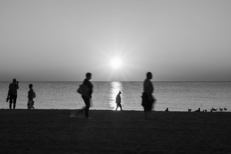 Blurry Silhouettes Of People Walking On Beach At Sunset Over Calm Seascape Horizon, Peaceful Morning Or Evening Travel Sceneの写真素材