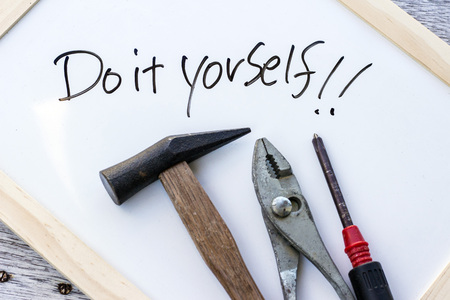 Do it yourself written on a whiteboard and a hammer, a pliers and a driver