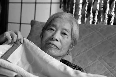 Elderly woman reclining on the nursing bed playing with blanket, close-up portraitの写真素材