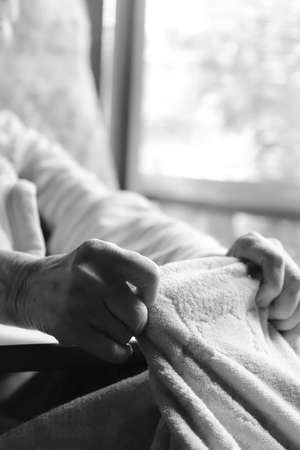 Hands of an elderly woman with dementia playing with a blanket in a nursing bed