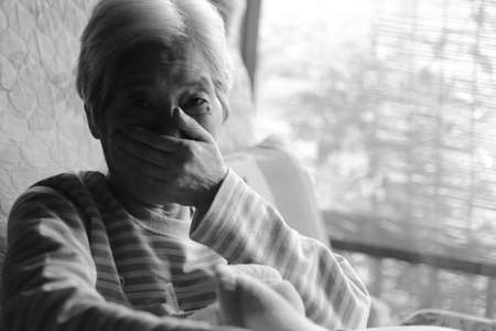 An elderly woman who covers her mouth with her hand while relaxing in a nursing bed
