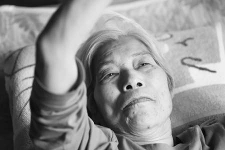 Close-up of the face of a senior woman with dementia who lies on a nursing bed and looks dazzlingの写真素材