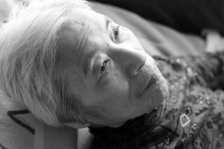 Close-up of a senior woman with dementia lying on a nursing bed and making a serious expressionの写真素材