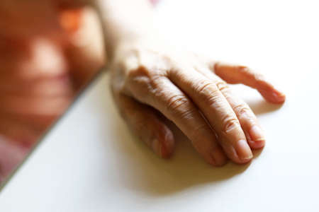 An elderly woman lying on a nursing bed and placing her hand on the nursing tableの写真素材
