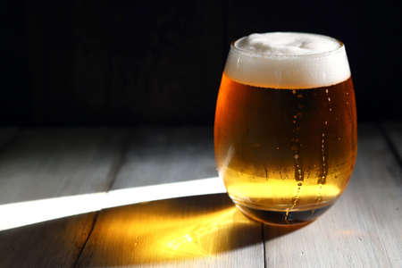 A frothy beer poured into a short, rounded glass illuminated by the strong afternoon lightの写真素材