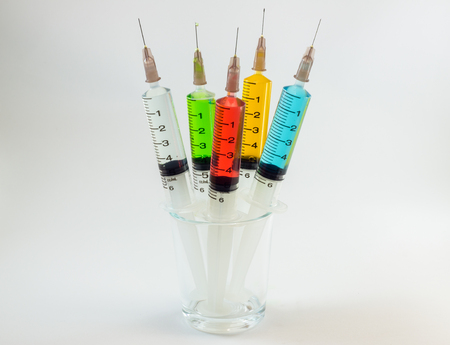 plastic medical syringes containing multicolor solutions in medicine glass with white backgroundの写真素材