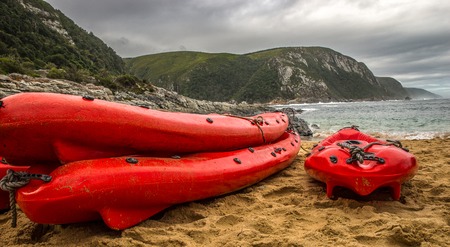 Three fire-red canoes are waiting on a quiet beach until they are used again. In the background the sea is visible, and the sky is cloudy.の写真素材