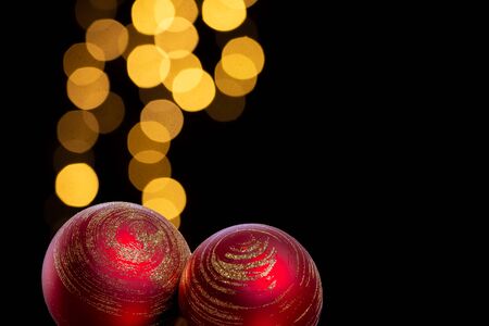 Two red Christmas baubles with golden decoration in a dark environment with blurred Christmas lights in the background. Christmas greetings card decorationの写真素材