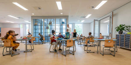 ARNHEM / NETHERLANDS - AUGUST 28 2020: Children in primary school work together in groups. They are located in a modern school buildingのeditorial素材