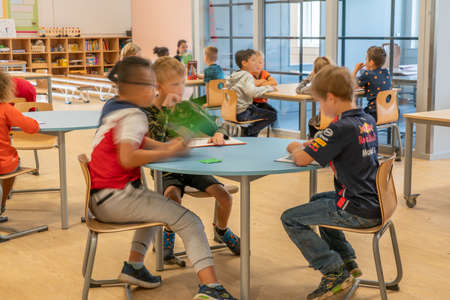 ARNHEM / NETHERLANDS - AUGUST 28 2020: Children in primary school work together in groups. They are located in a modern school buildingのeditorial素材
