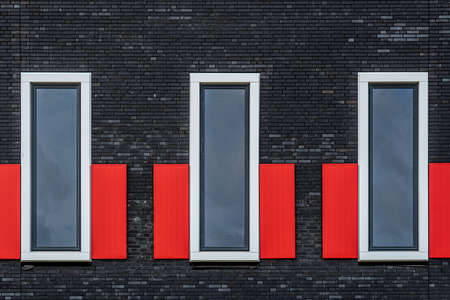 Fragment of a modern building facade with three windows in a row. Brick facade and red shutters
