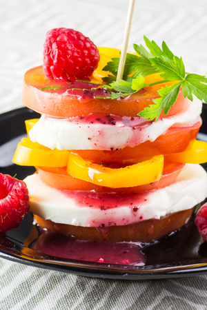 Closeup of tomato stack salad with fresh mozzarella, pepper and raspberry dressing on a black plate.の写真素材