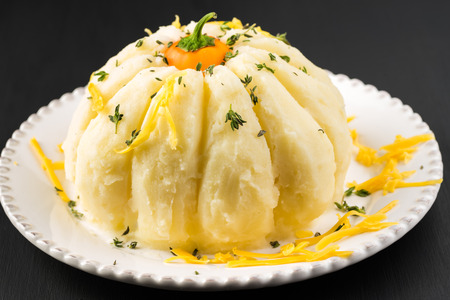 Close up of pumpkin shaped mashed potatoes on black background.